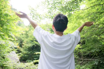 緑の中で深呼吸する少年や青年の夏休みなどのイメージ顔無しの後ろ姿