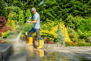 Man Using Pressure Washer to Clean Patio in a Vibrant Garden on a Sunny Day