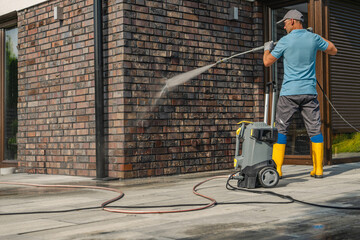Man Using Pressure Washer to Clean Brick Wall of Modern House During Daytime