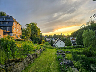 Obraz premium peaceful town of hartenstein, saxony, scene at sunset with lush greenery, charming houses, and a golden sky casting warm light over the serene landscape