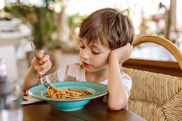 Young boy thoughtfully eating spaghetti at a restaurant table, enjoying a quiet meal...