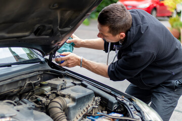 A young man spraying and lubricating rusty screw with a chemical agent. Mechanic's hand working under open hood of car.