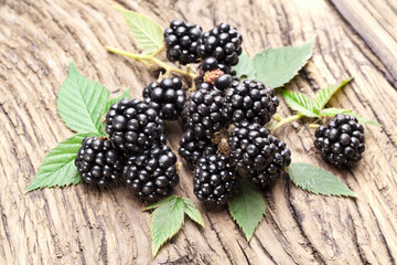 Blackberries with green leaves on old wooden background.