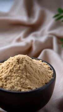 Aromatic maca powder in a black bowl, cinnamon sticks, and fresh green herbs on a textured fabric backdrop
