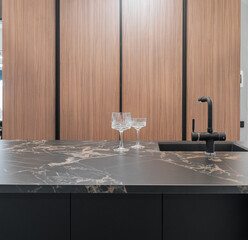 modern built-in kitchen. kitchen island with black marble countertop. Kitchen with wooden doors. beautiful wine or champagne glasses on the countertop.
