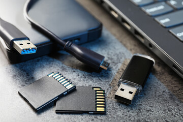 SD memory cards, USB flash drive, hard disk drive with cable and laptop on dark grey table, closeup