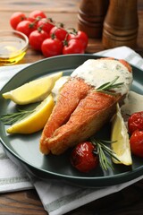 Seafood. Tasty salmon steak served with sauce, tomatoes, rosemary and lemon on wooden table, closeup