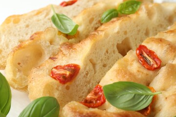 Cut delicious focaccia with tomatoes and basil on table, closeup