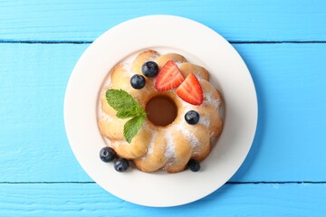 Tasty Bundt cake with powdered sugar and berries on light blue wooden table, top view