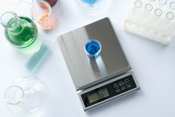 Scale with beaker of sample and other laboratory equipment on white background, flat lay
