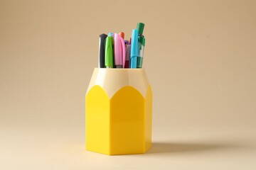 Pencils and pens in holder on beige background
