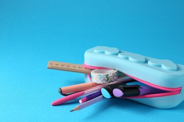 Different stationery in pencil case on light blue background, closeup. Space for text