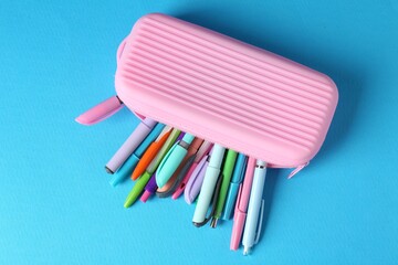 Pencils and pens in case on light blue background, top view