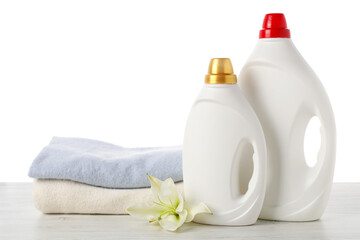 Bottles of fabric softener, stacked clothes and flower on wooden table against white background