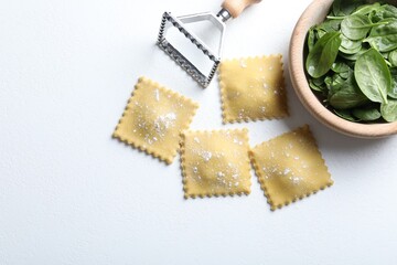 Uncooked ravioli, cutter and spinach on white table, flat lay. Space for text