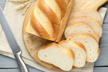 Sliced bread and knife on grey wooden table, flat lay