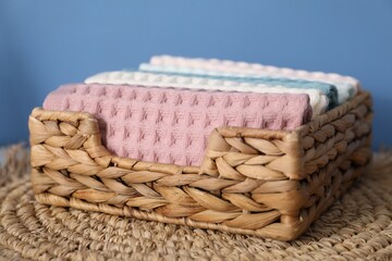 Clean waffle towels in wicker basket on mat near blue wall, closeup