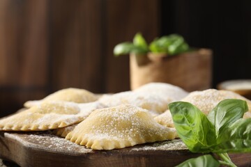 Uncooked ravioli and basil on wooden table, closeup. Space for text