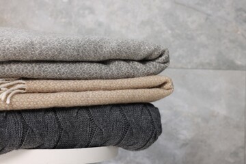 Folded woolen plaids on table near grey wall, closeup