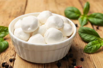 Mozzarella cheese balls with basil and peppercorns on wooden table, closeup