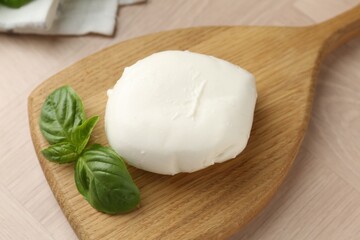 Piece of delicious mozzarella cheese and basil on wooden table, closeup