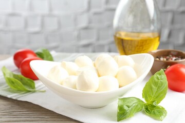 Tasty mozzarella cheese balls, tomatoes, basil, oil and peppercorns on wooden table, closeup