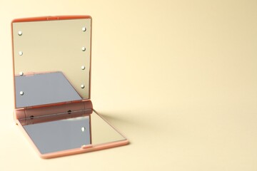 Open pocket mirror on beige background, closeup. Space for text