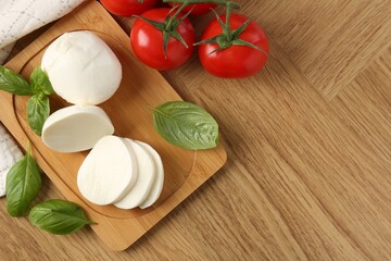 Tasty mozzarella, tomatoes and basil on wooden table, flat lay. Space for text