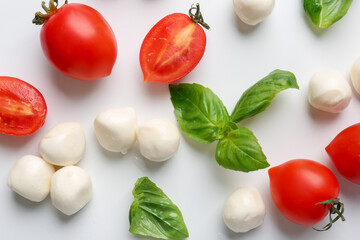 Tasty mozzarella balls, tomatoes and basil on white background, flat lay