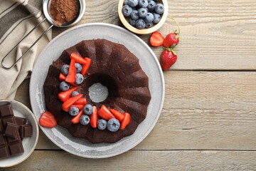 Tasty chocolate bundt cake with berries on wooden table, flat lay