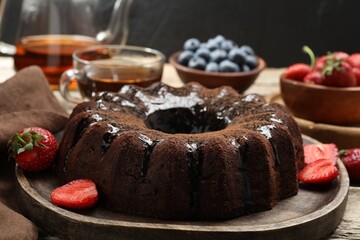 Tasty chocolate bundt cake with glaze, tea and berries on wooden table, closeup
