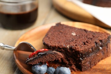 Piece of delicious chocolate bundt cake with blueberries on wooden table, closeup