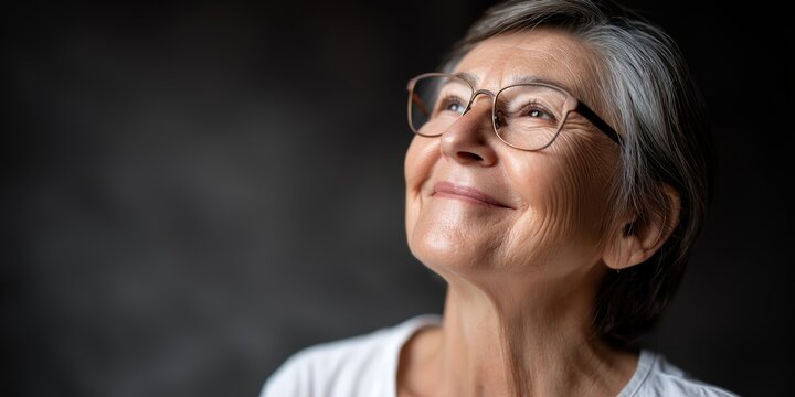 A friendly older woman with soft round features, wearing glasses and smiling gently. 