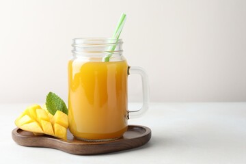 Tasty mango juice in glass mason jar, fresh fruit and mint on white table, space for text