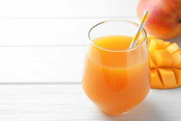 Tasty mango juice in glass and fresh fruits on white wooden table, closeup. Space for text