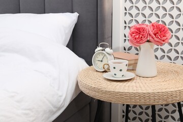Side table with alarm clock, cup of tea, books and decor near bed indoors