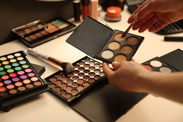 Woman with brush and eyeshadow palette at dressing table, closeup