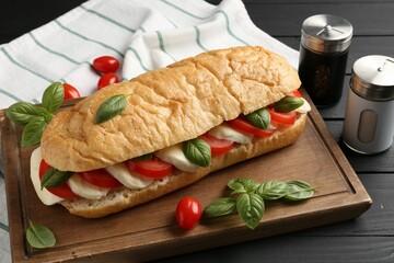 Tasty sandwich with mozzarella cheese, tomatoes and basil on black wooden table, closeup
