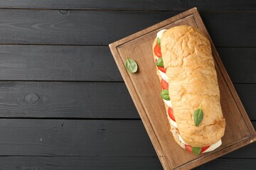 Tasty sandwich with mozzarella cheese, tomatoes and basil on black wooden table, top view. Space...