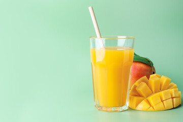 Tasty mango juice in glass and fresh fruits on green background, space for text