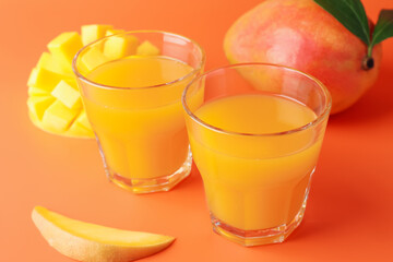 Tasty mango juice in glasses and fresh fruits on orange background, closeup