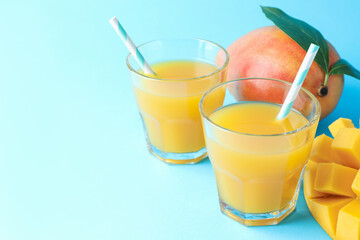 Tasty mango juice in glasses and fresh fruits on light blue background, closeup. Space for text