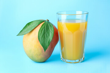 Tasty mango juice in glass and fresh fruit on light blue background