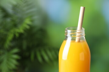 Tasty mango juice in glass bottle on blurred background, closeup. Space for text