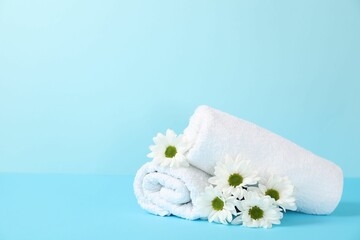 Soft towels and chrysanthemum flowers on light blue background, space for text