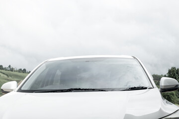 Windshield on a white car, top front part of white parked car against sky.