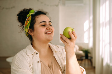 Portrait of a young smiling curly-haired plus-size woman with apple in her hands.Healthy eating and healthy lifestyle.