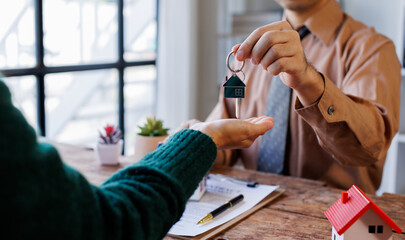 Real estate agent giving house key to the client after signing making sign insurance form agreement, the real estate contract. Home and real estate trading concept.
