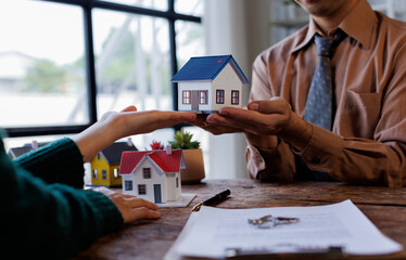 Real estate transaction with agent holding home model, investment small miniature white toy house....