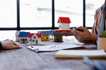 Real estate transaction with agent holding home model, investment small miniature white toy house....
